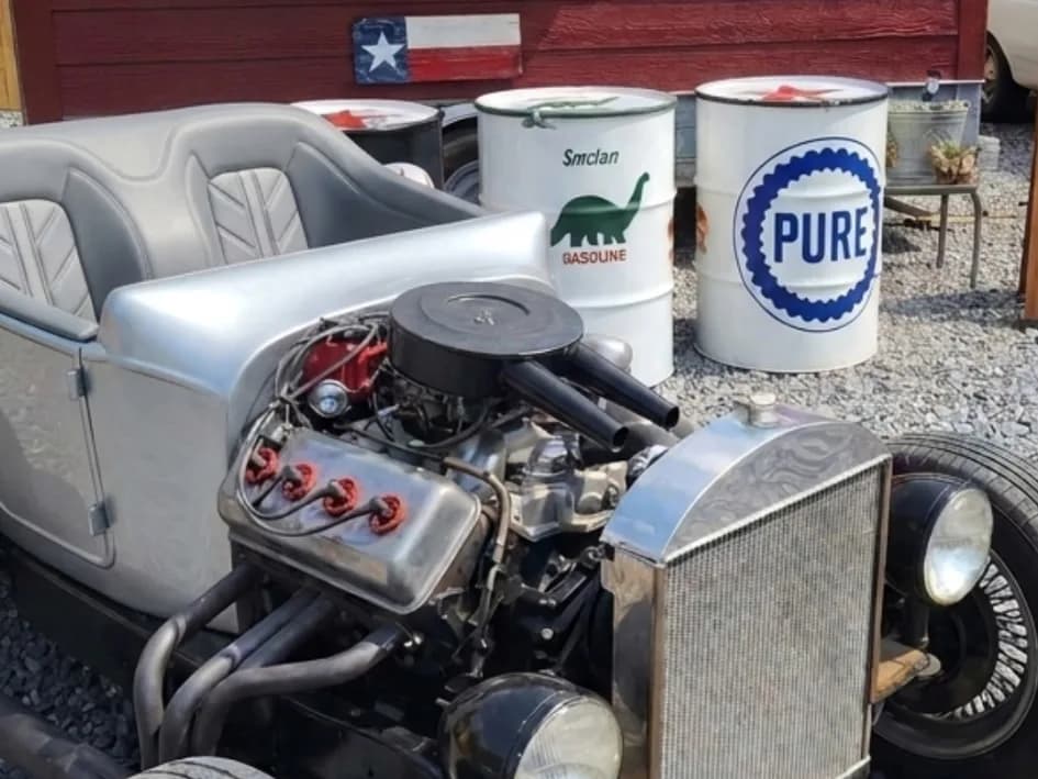 A silver hot rod's chrome V8 engine next to vintage Sinclair and Pure oil drums at Yabba Dabba Dogs